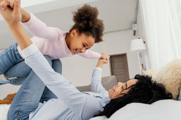 Madre jugando con su hija sonriente en la cama en casa