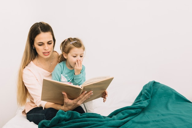 Madre leyendo el libro a la hija soñolienta