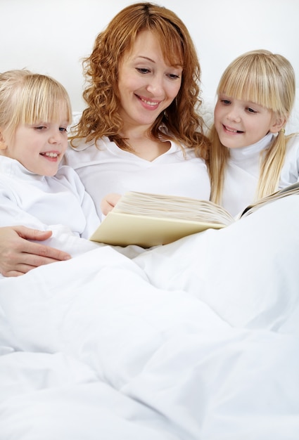 Madre leyendo a sus hijas en la cama