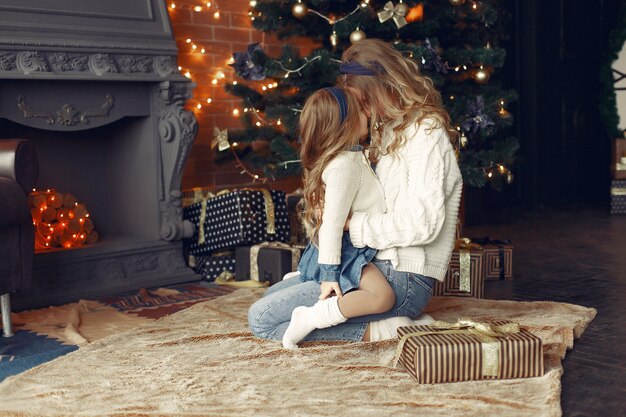 Madre con linda hija en casa junto a la chimenea