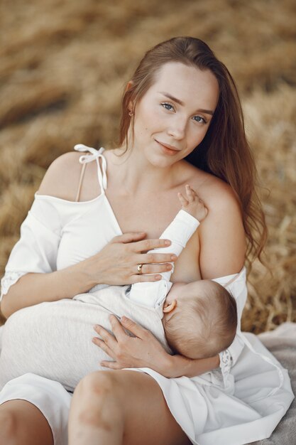 Madre con linda hija. Mamá amamantando a su pequeña hija. Mujer con un vestido blanco.