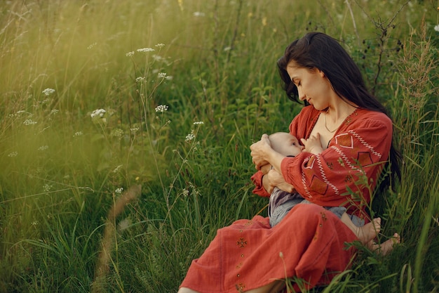 Madre con linda hija. Mamá amamantando a su pequeño hijo. Mujer con un vestido rojo.