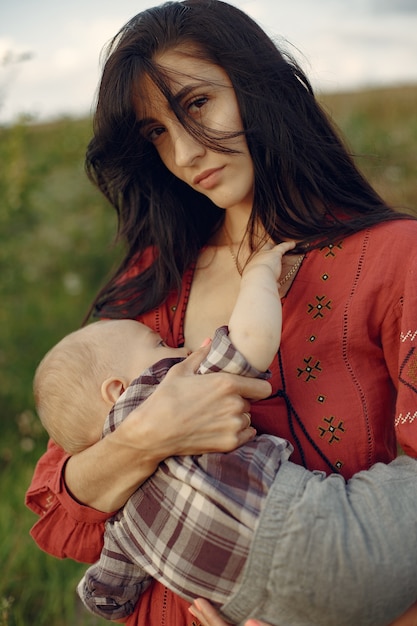 Madre con linda hija. Mamá amamantando a su pequeño hijo. Mujer con un vestido rojo.