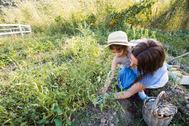 Madre llevando a su niña cosechando vegetales en el campo