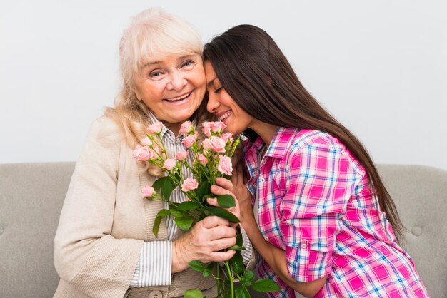 Madre mayor sonriente que inclina su cabeza en el hombro de su madre mayor que sostiene rosas