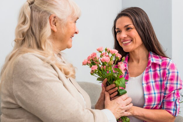 Madre mayor sonriente y su hija que sostienen el ramo color de rosa