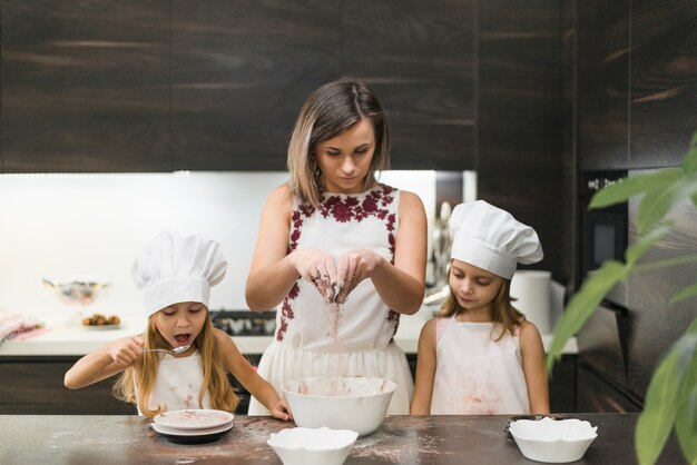 Madre mezclando cacao en polvo para hacer galletas con sus hijas en la cocina