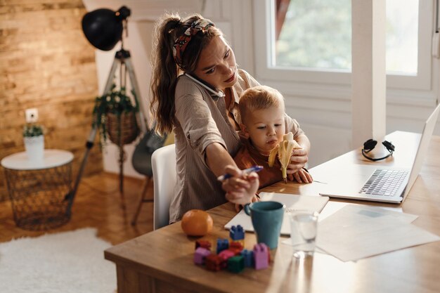 Madre multitarea cuidando a su pequeño hijo mientras trabaja en casa