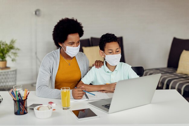 Madre negra e hijo usando una computadora portátil mientras estudian en casa durante la epidemia de coronavirus