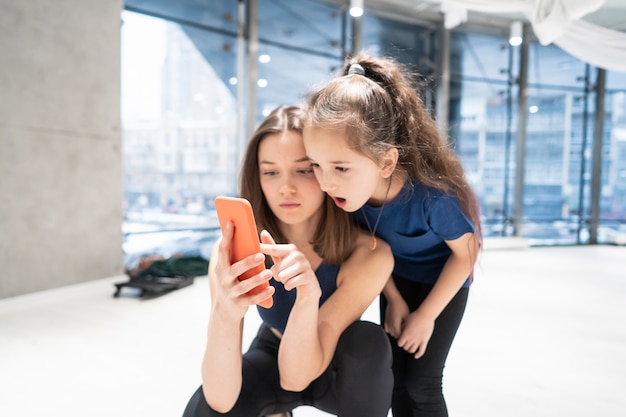 Madre y niña usando el teléfono en el gimnasio para ver videos
