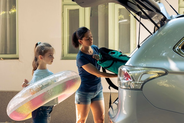 Madre con niño cargando equipaje en el maletero, preparándose para partir en viaje por carretera. Mujer y niño pequeño viajando de vacaciones en la playa durante el verano, feliz recreación.