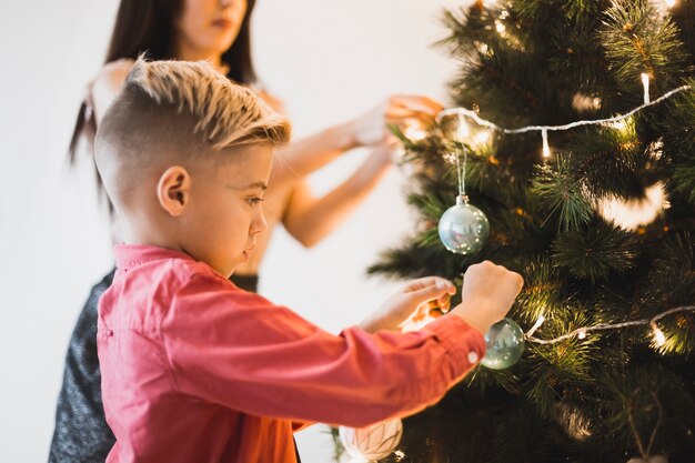 Madre y niño decorando árbol de navidad iluminado