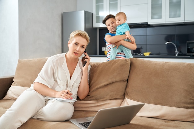 Madre ocupada trabajando en casa mientras sus hijos juegan cerca