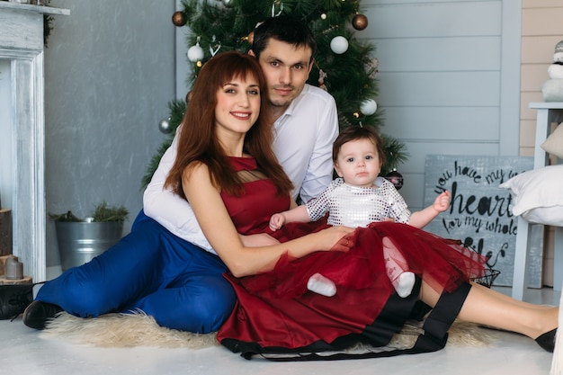 La madre, el padre y la hija sentados cerca del árbol de Navidad