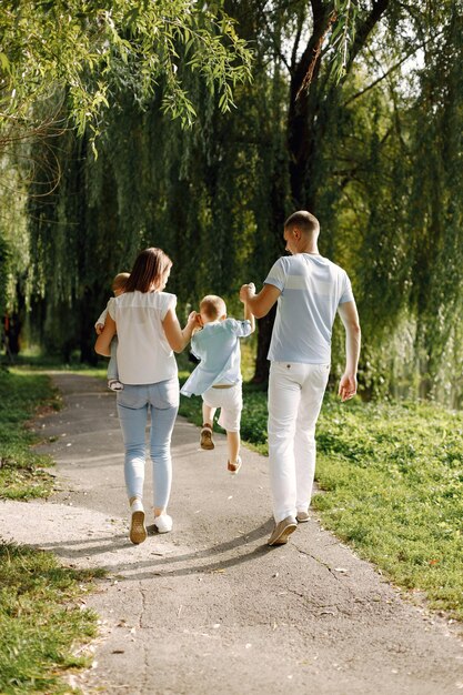 Madre, padre, hijo mayor y pequeña hija caminando en el parque. Familia vistiendo ropa blanca y azul claro