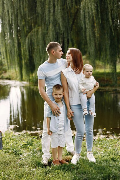 Madre, padre, hijo mayor y pequeña hija caminando en el parque. Familia vistiendo ropa blanca y azul claro