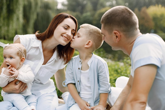 Madre, padre, hijo mayor y pequeña hija sentada en el parque. Familia vistiendo ropa blanca y azul claro