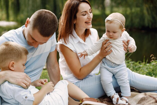 Madre, padre, hijo mayor y pequeña hija sentada sobre una alfombra de picnic en el parque. Familia vistiendo ropa blanca y azul claro