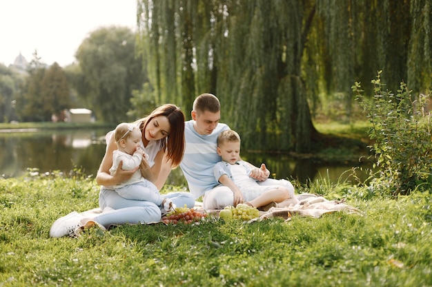 Madre, padre, hijo mayor y pequeña hija sentada sobre una alfombra de picnic en el parque. Familia vistiendo ropa blanca y azul claro