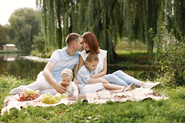 Madre, padre, hijo mayor y pequeña hija sentada sobre una alfombra de picnic en el parque. Familia vistiendo ropa blanca y azul claro