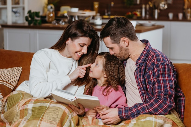 Madre y padre leyendo libro con hija en el sofá