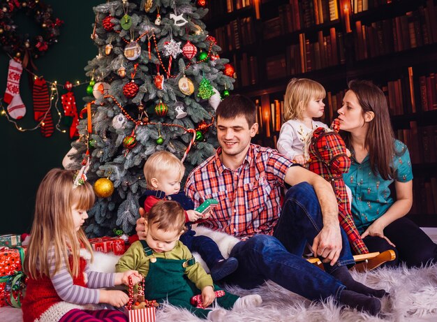 La madre, el padre y los niños sentados cerca del árbol de Navidad