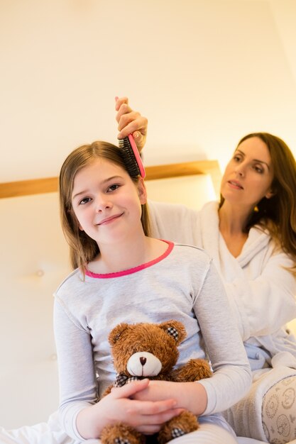 La madre peina el pelo hijas en el dormitorio