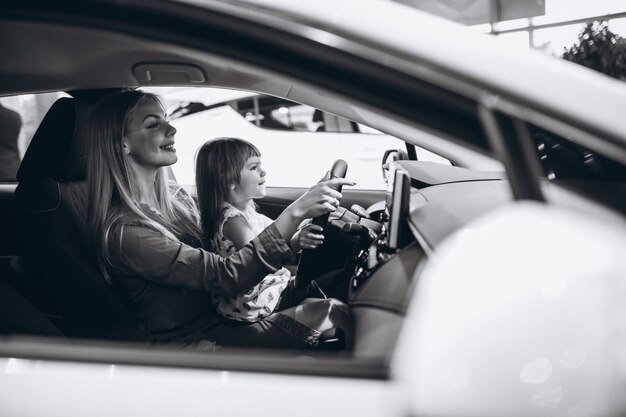 Madre con pequeña hija sentada en un automóvil en una sala de exposición de automóviles