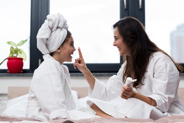 Madre poniendo crema para el cuidado de la piel en la cara de su hija