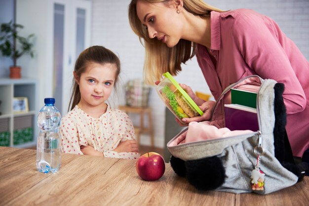 Madre poniendo lonchera con comida sana en la mochila de la hija