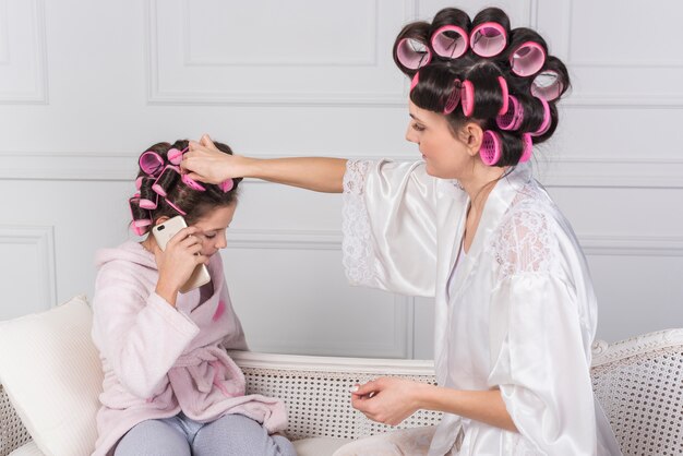 Madre poniendo rizador rosa en el pelo de hijas