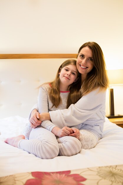 Madre que abraza a la hija en el dormitorio