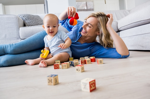 Madre que mira al bebé jugando con juguetes en la sala de estar