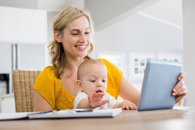 Madre que mira a la tableta digital con el bebé en la cocina