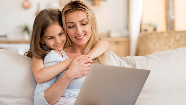 Madre que trabaja en la computadora portátil desde casa con la hija abrazándola