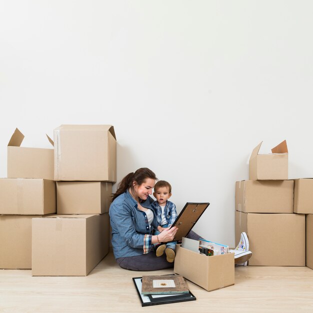 Madre sentada con su hijo mirando el marco de la foto desempacando las cajas de cartón