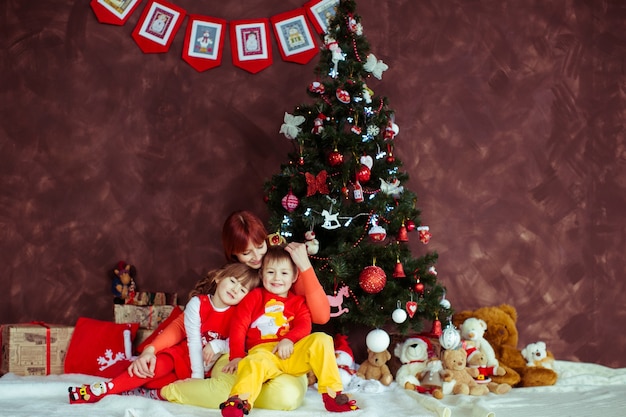 La madre se sienta con sus hijos antes de un árbol de Navidad