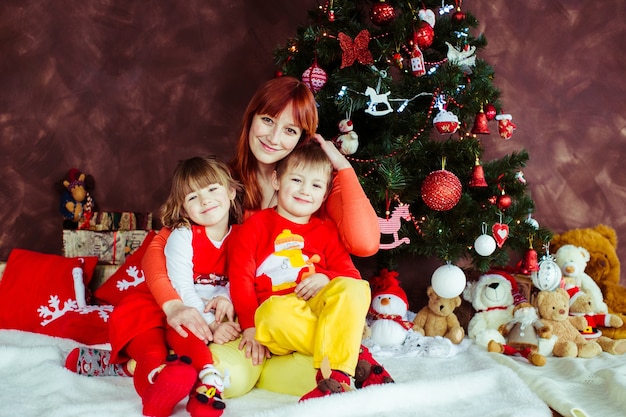 La madre se sienta con sus hijos antes de un árbol de Navidad