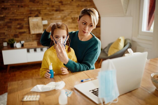 Madre soltera que le da tratamiento de asma a su pequeña hija mientras usa una laptop en casa