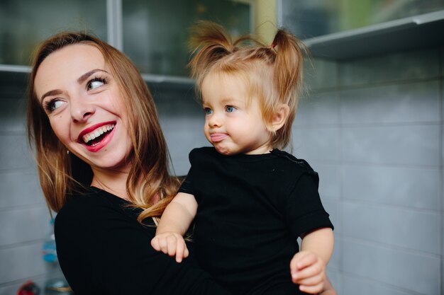 Madre sonriendo con su hija en brazos y la niña con la lengua fuera