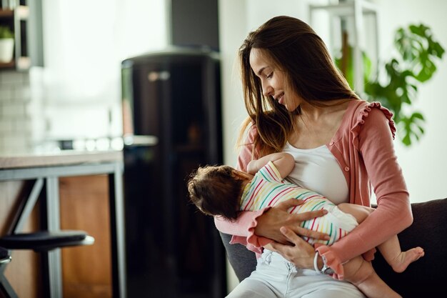 Madre sonriente amamantando a su hija mientras está en casa