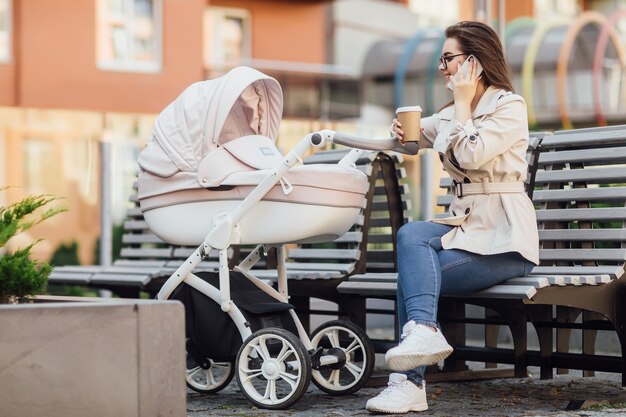 Madre sonriente con un bebé recién nacido en un cochecito bebe té o café en una calle