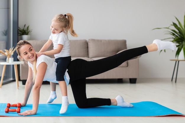 Madre sonriente haciendo ejercicio en casa con hija