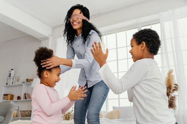 Madre sonriente jugando con sus hijos en casa con los ojos vendados