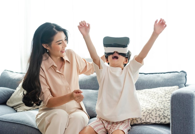 Madre sonriente mirando a su hijo jugando con auriculares de realidad virtual VR en casa