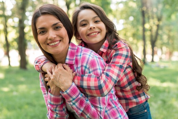 Madre sonriente que da a cuestas paseo a su hija en el parque