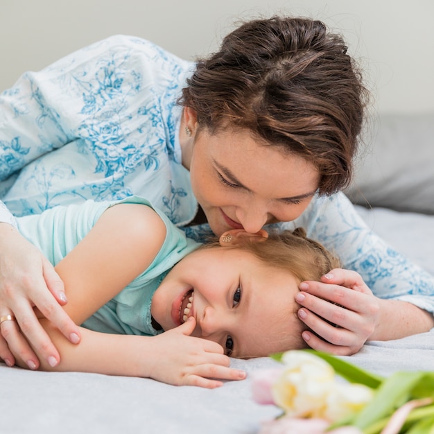 Madre sonriente que susurra en el oído de su pequeña hija en la cama