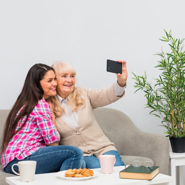 Madre sonriente y su hija joven que toman el selfie en el teléfono celular en casa