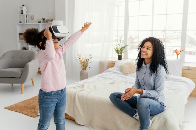 Madre sonriente viendo a su hija jugar con casco de realidad virtual