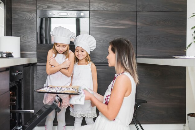 Madre sosteniendo galletas horneadas en bandeja mientras mira a sus hijas